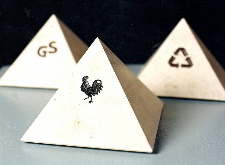 Gruppe von drei Pyramiden aus geschliffenem  Jura-Kalkstein, die vorderste hat ein  Piktogramm eingraviert, das den gallischen  Hahn darstellt