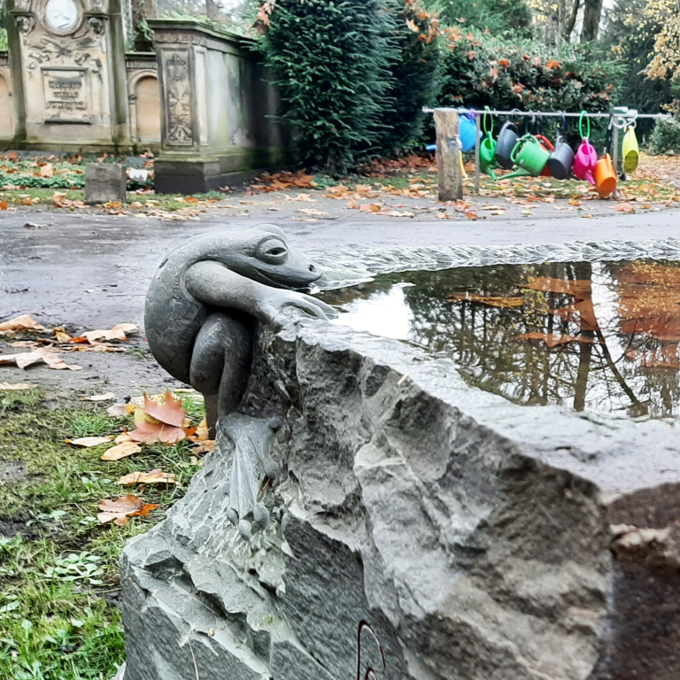 Vogeltränke aus Bergischer Grauwacke mit  vollplastisch gearbeiteter Frosch-Skulptur, zu  sehen auf dem Friedhof Melaten in Köln