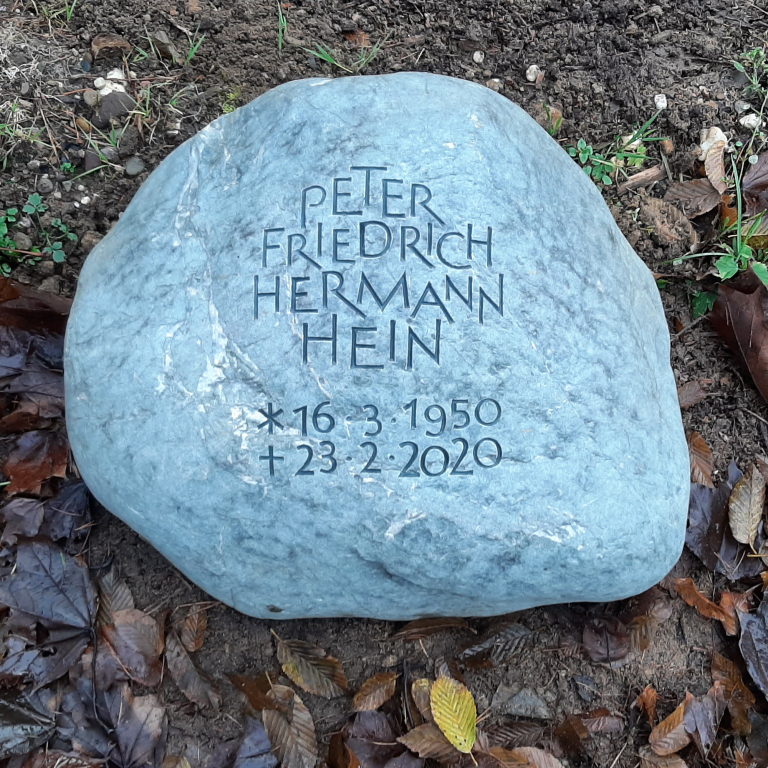 Bläulicher Grabstein-Findling für ein Urnengrab mit ornamental  angeordneter, genuteter Grotesk-Schrift