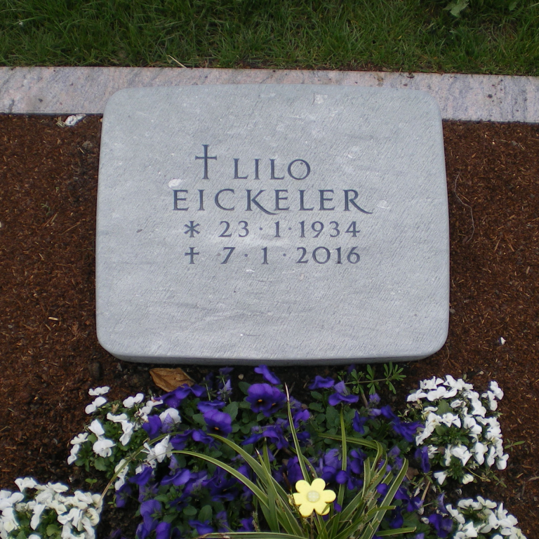 Gebrauchter, neu aufgearbeiter, liegender Grabstein mit eingehauener Schrift und einem Kreuz-Ornament