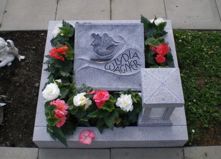 Quadratischer Urnen-Grabstein mit handwerklicher Oberfläche und Tauben-Ornament aus belgischem Blaustein, umgeben von einer Grabumrandung