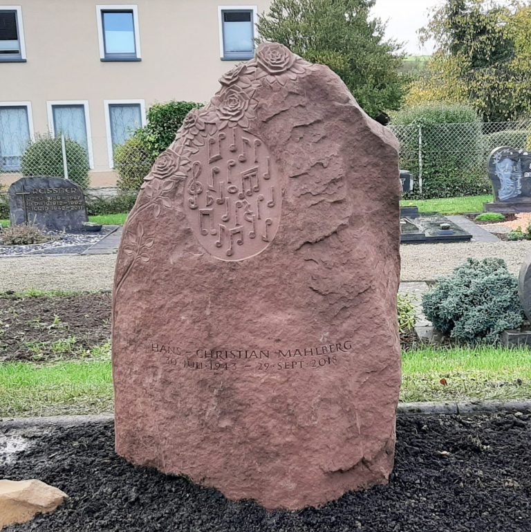 Natürlich gebrochenes Felsen-Grabmal aus rotem Eifel-Sandstein mit in den Stein gehauenem Rosen-Ornament und erhabenen Noten