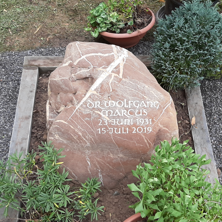 Grau-weiß-braun marmorierter Findling-Grabstein für ein  Einzelgrab mit eingehauener, getönter Unzialis-Beschriftung und  Grabumrandung aus Bergischer Grauwacke