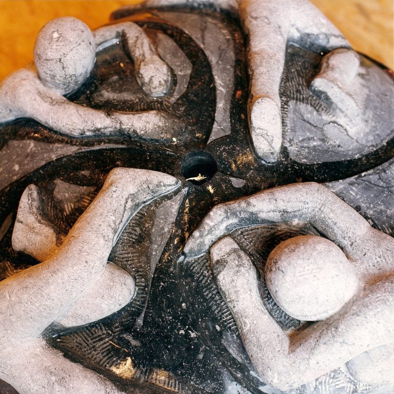 Brunnen-Skulptur aus belgischen Blaustein mit  vier Gestalten, die an einer rundlichen, glatten  Oberfläche sich festhalten zu wollen scheinen