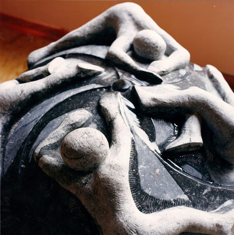 Brunnen-Skulptur aus belgischen Blaustein mit  vier Gestalten, die an einer rundlichen, glatten  Oberfläche sich festhalten zu wollen scheinen