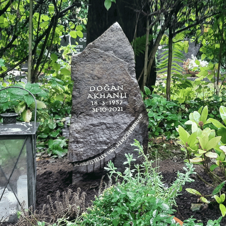 Bauchig gebrochener Felsen aus Ruhrsandstein, Grabstein von Dogan Akhanli, mit vertieft genuteter Schrift und dem Sinnspruch Schriftsteller und Menschenfreund