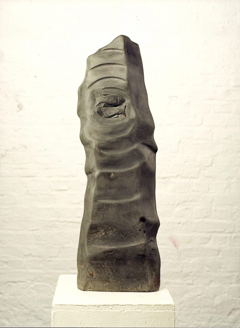 Dunkel geschliffene Basaltsäule mit einem  Fisch-Ornament und einer welligen  Ansichtsfläche