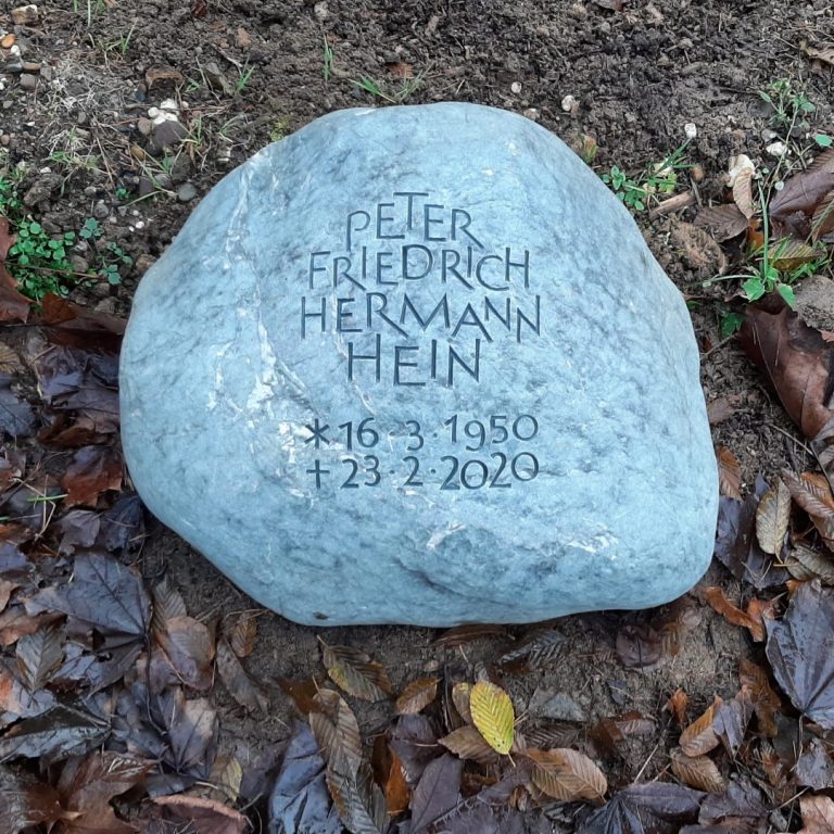 Bläulicher Grabstein-Findling für ein Urnengrab mit ornamental  angeordneter, genuteter Grotesk-Schrift