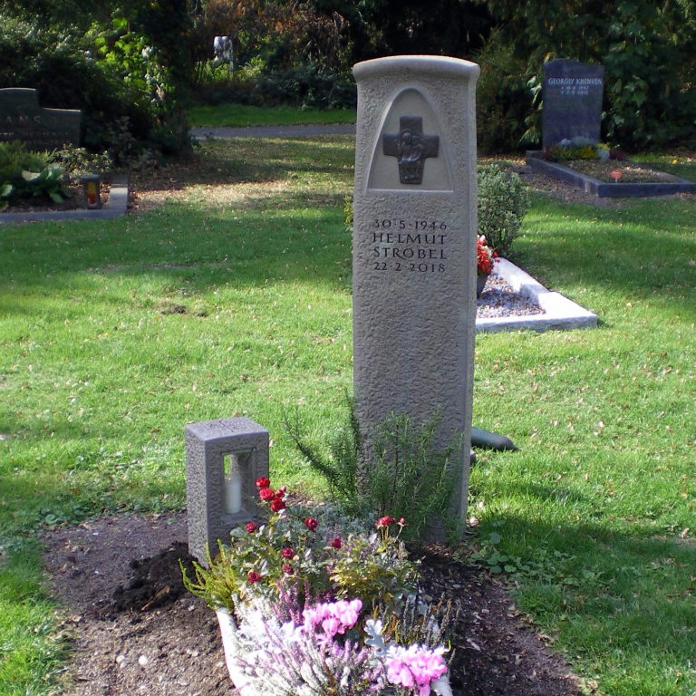 Grabstele aus Bergischer Grauwacke mit vom Steinmetzen erarbeiteter Oberfläche und Bronzekreuz in Parabelförmiger Vertiefung