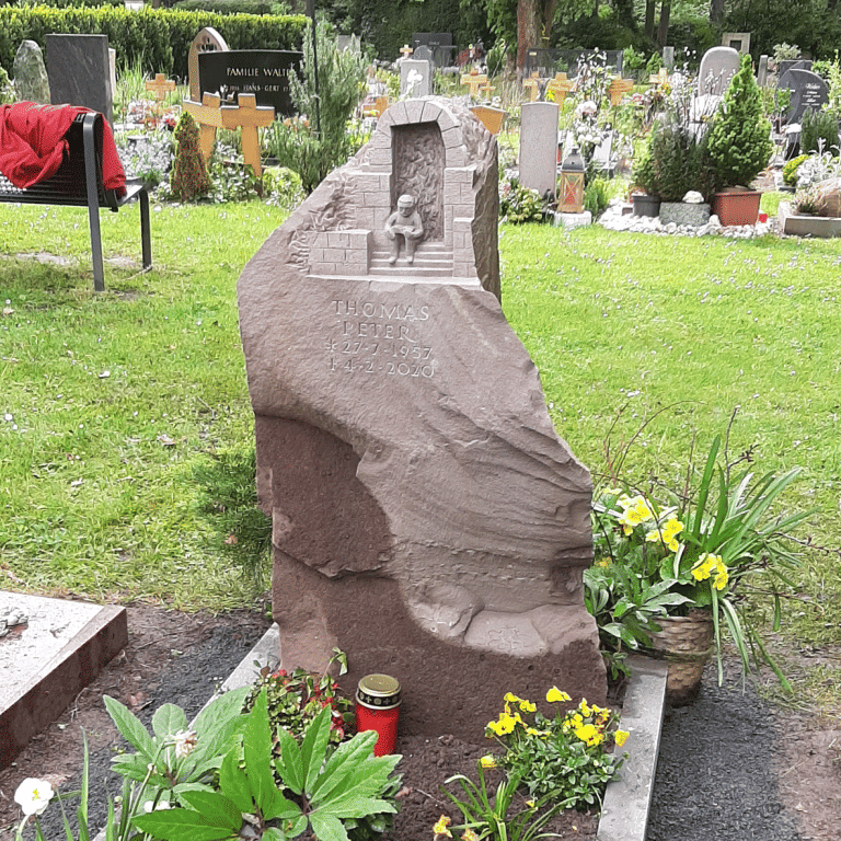 Grabstein aus bergischer Grauwacke mit dreidimensionalem Ornament, welches einen lesenden Mann vor dem römischen Kölner Nordtor darstellt
